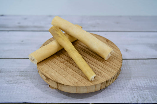 Three cow tail sticks for dogs on a round wooden board.|Trois bâtonnets de queue de bœuf pour chiens sur une planche en bois ronde.