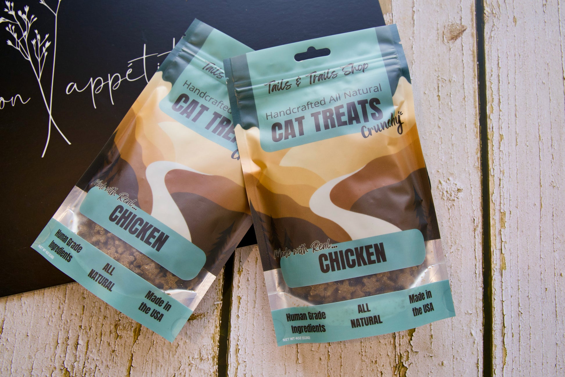 Deux paquets de friandises au poulet pour chats sur une surface en bois, sur fond sombre.