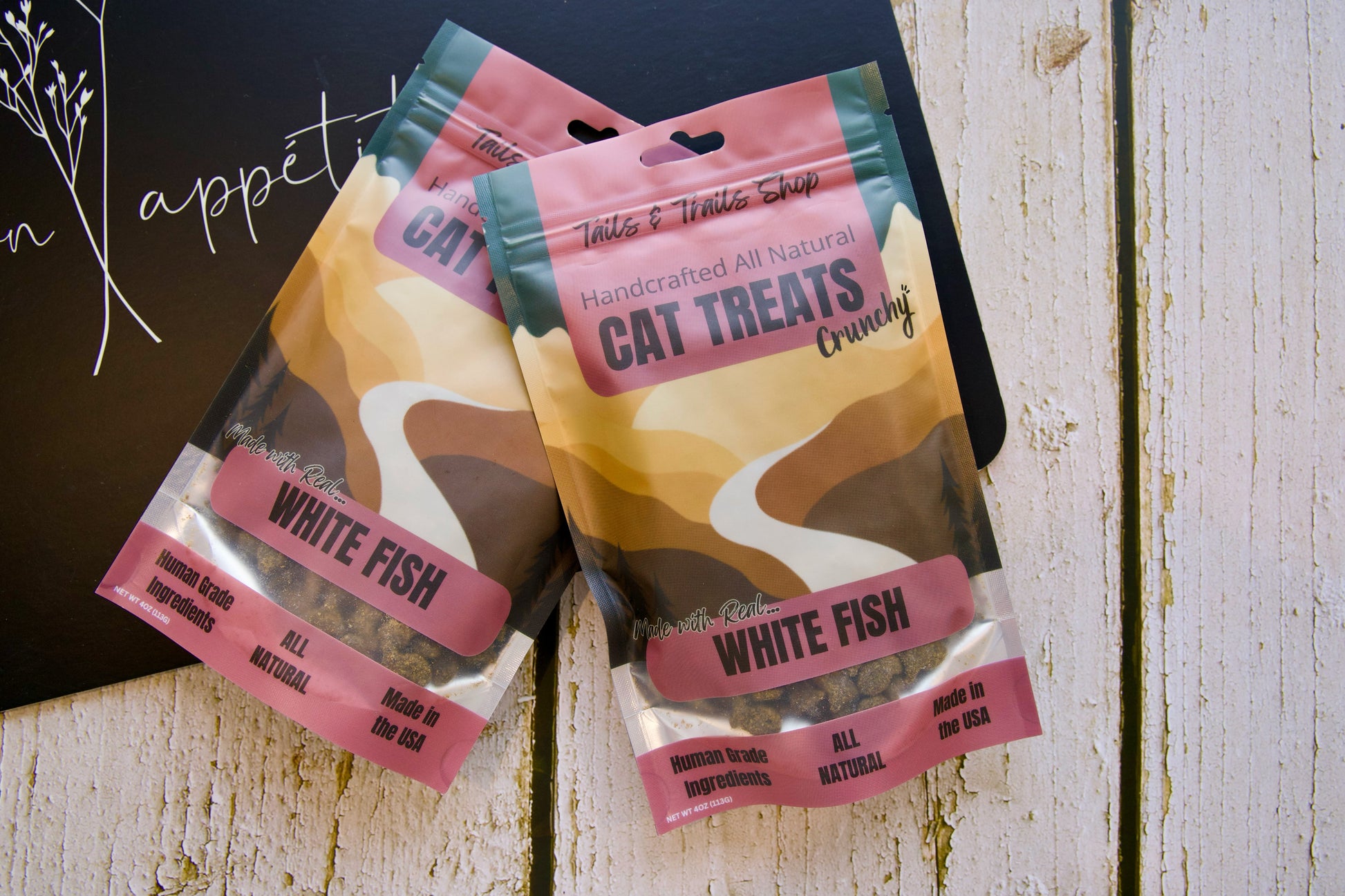 Deux paquets de friandises pour chats au poisson blanc sur une surface en bois.