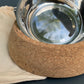 Cork base with a metal bowl for pets on a gray background.
