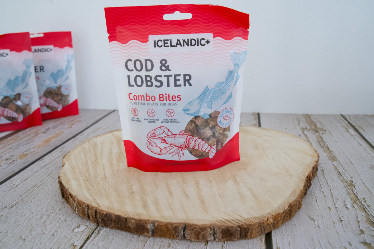 Un paquet de friandises pour chiens Icelandic+ à base de morue et homard présenté sur une planche en bois ronde.