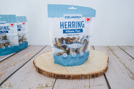 Un sachet de friandises naturelles pour chiens Icelandic+ (harengs entiers) est posé sur une planche en bois ronde.