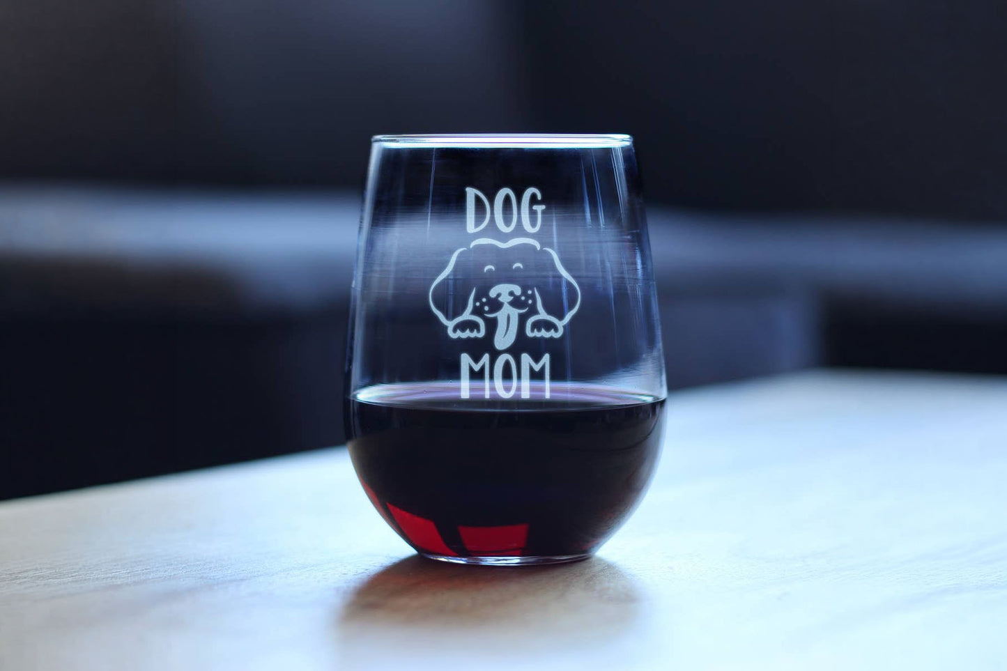 Stemless wine glass with 'DOG MOM' engraving on a table.
