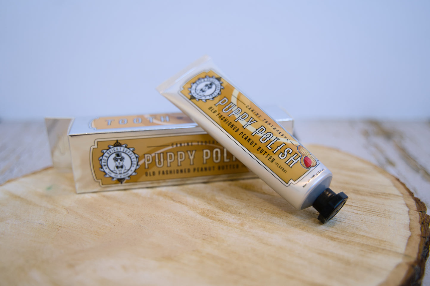 Deux tubes de dentifrice pour chiens Puppy Polish posés sur une surface en bois avec un fond bleu clair.