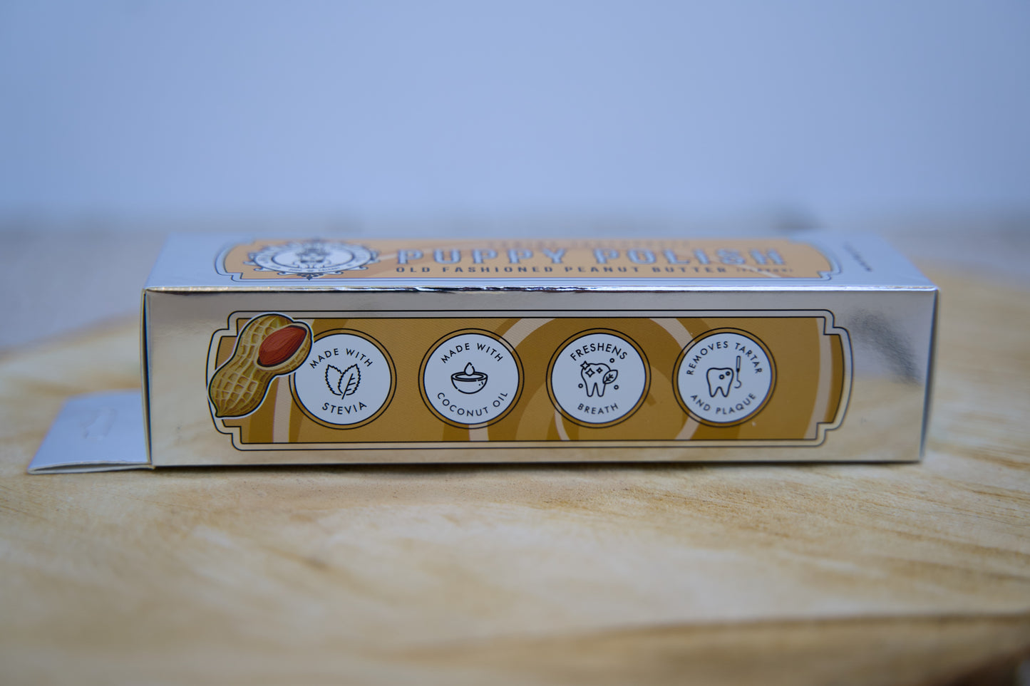 Boîte de dentifrice pour chien avec la marque et les informations sur les ingrédients, posée sur une surface en bois.