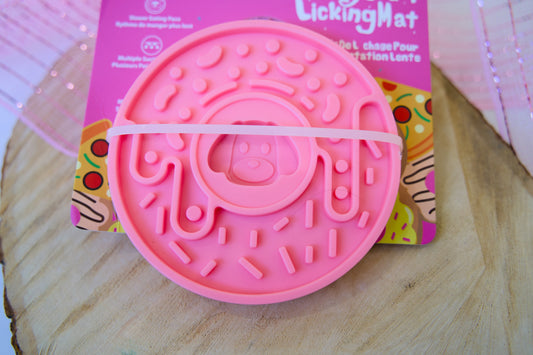 Donut-shaped pink pet licking mat on a wooden surface.|Tapis de léchage rose en forme de beignet pour animaux de compagnie, posé sur une surface en bois.