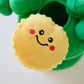 Plush dog toy with a smiley face design held by green gloves on a white background.