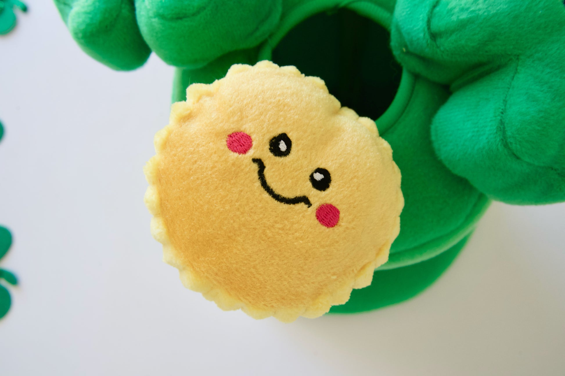 Plush dog toy with a smiley face design held by green gloves on a white background.