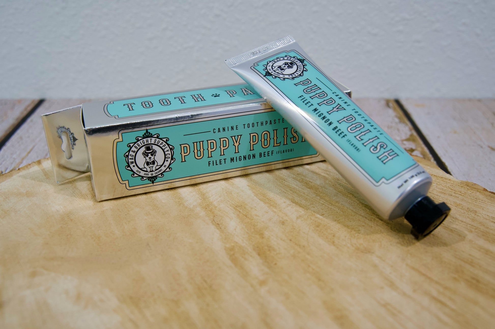 Tube et emballage de dentifrice pour animaux Puppy Polish (saveur filet mignon) posés sur une surface en bois.