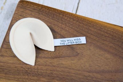 A fortune cookie cat toy with catnip and a tag that reads YOU WILL MISS THE LITTER BOX.