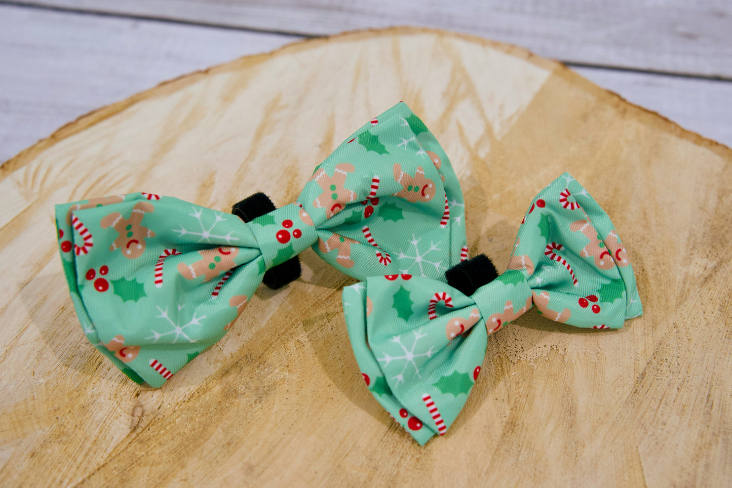 Deux nœuds papillon verts pour chien à motifs festifs de Noël sur une surface en bois.