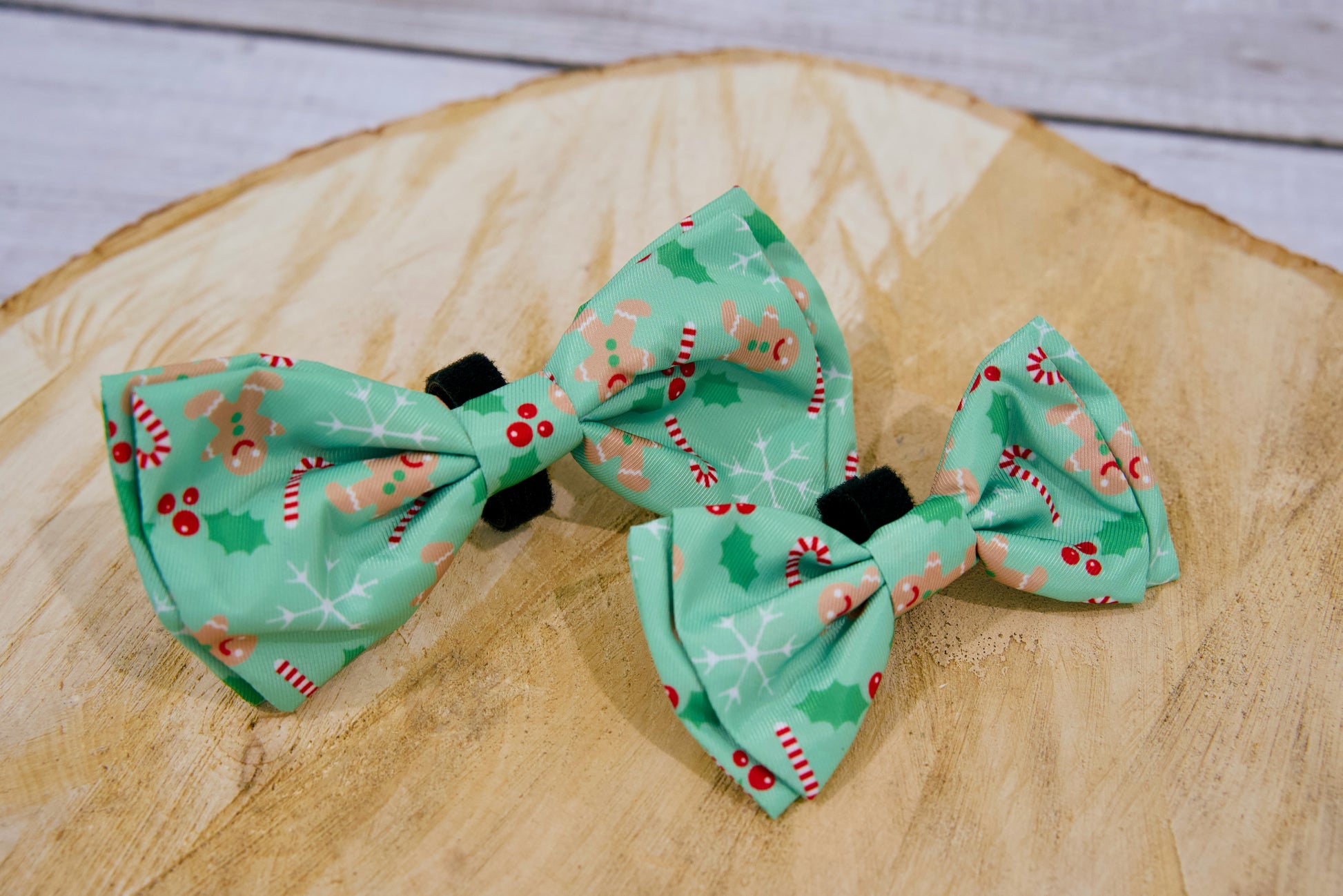 Deux nœuds papillon verts pour chien à motifs festifs de Noël sur une surface en bois.
