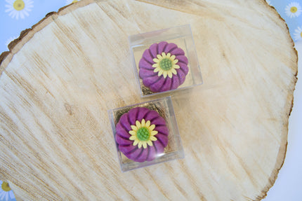 Two purple flower-shaped dog treats in clear cases on a wooden surface with a floral background.