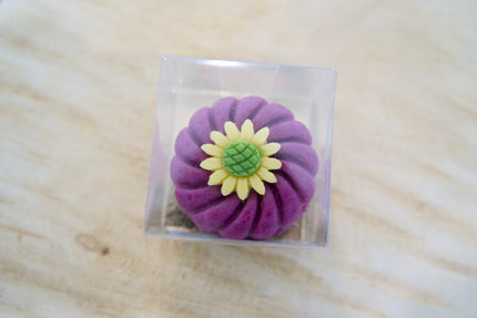Purple flower-shaped dog cake on a clear square base with a wooden surface background.