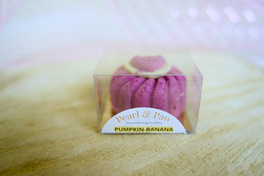 Pink dog treat pumpkin-banana in a clear packaging box on a wooden surface.|Friandises roses pour chiens à la citrouille et à la banane, présentées dans une boîte transparente sur une surface en bois.