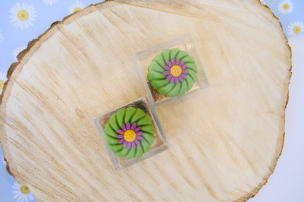 Des gâteaux pour chiens en forme de fleurs vertes et violettes, posés sur une surface en bois avec un fond floral.