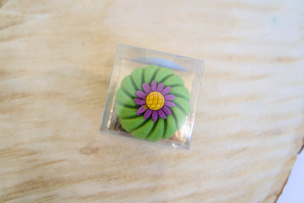 Friandise pour chien en forme de fleur verte, posée sur une base carrée transparente, elle-même placée sur une surface en bois.
