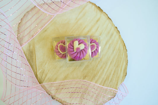 Pink dog cookies in clear cases on a decorative background.|Biscuits pour chiens roses présentés dans des boîtes transparentes sur un fond décoratif.