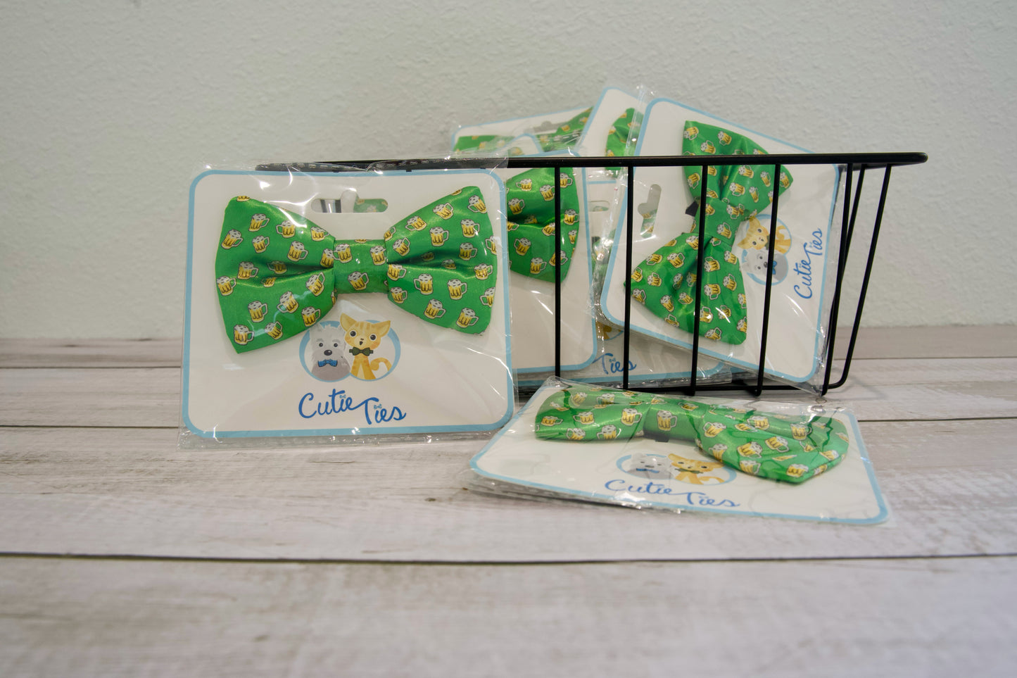 Nœuds papillon verts pour chiens, à motif de bière, dans un emballage étiqueté « Cute Ties », posés sur une surface en bois.