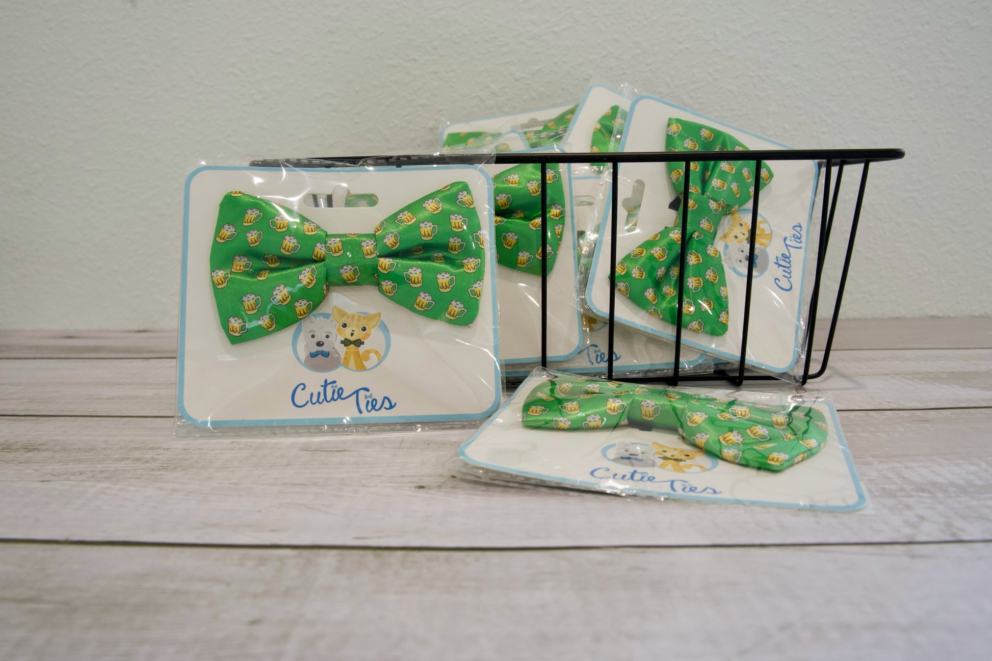 Nœuds papillon verts pour chiens, à motif de bière, dans un emballage étiqueté « Cute Ties », posés sur une surface en bois.