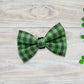 Green checkered dog bow tie on a wooden surface with shamrock leaves.
