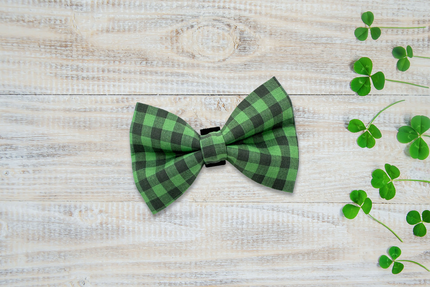 Green checkered dog bow tie on a wooden surface with shamrock leaves.