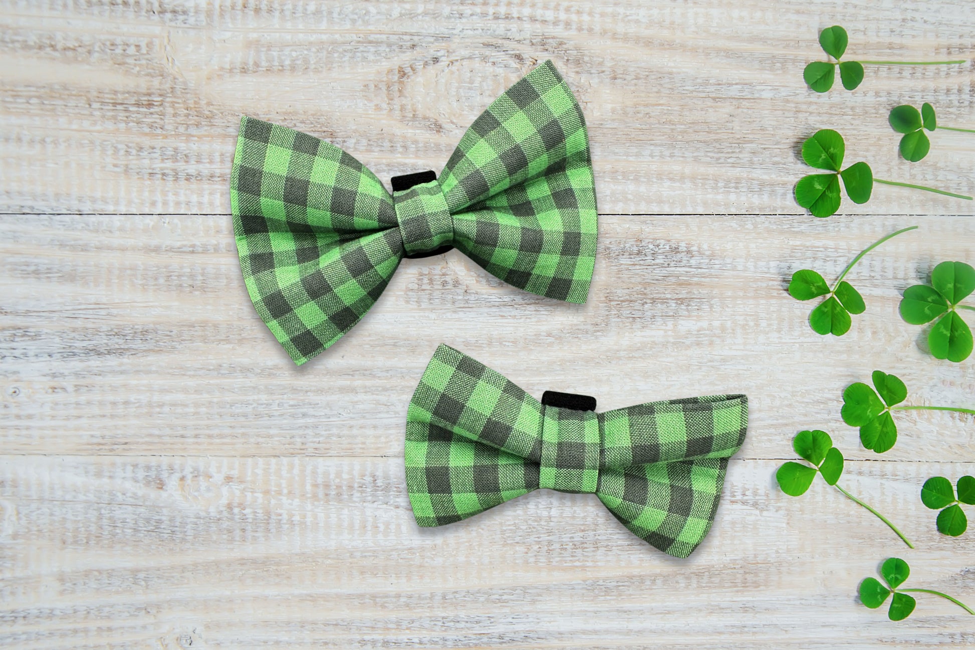 Two green and black checkered dog bow ties on a wooden surface with clover leaves.