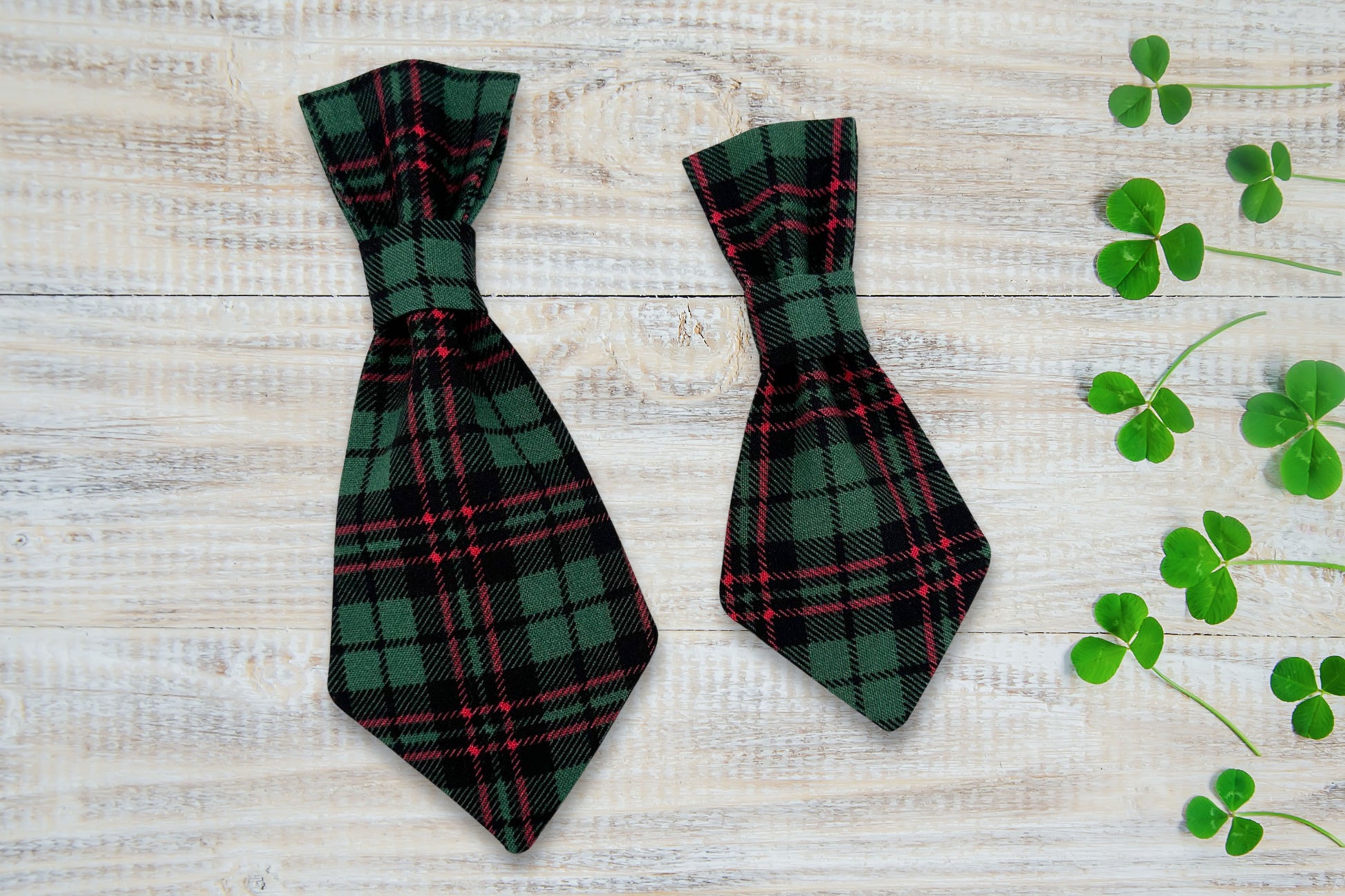 Two green plaid dog ties on a wooden surface with clover leaves.