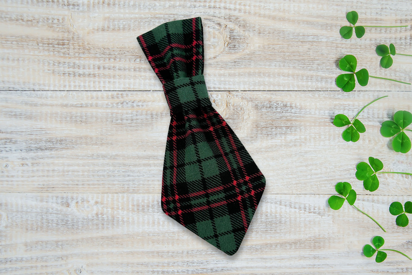 Plaid dog tie on a wooden surface with clover leaves.