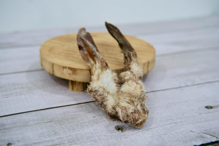 Une paire d'oreilles de lapin séchées pour chiens, avec les poils, présentée sur un support rond en bois.