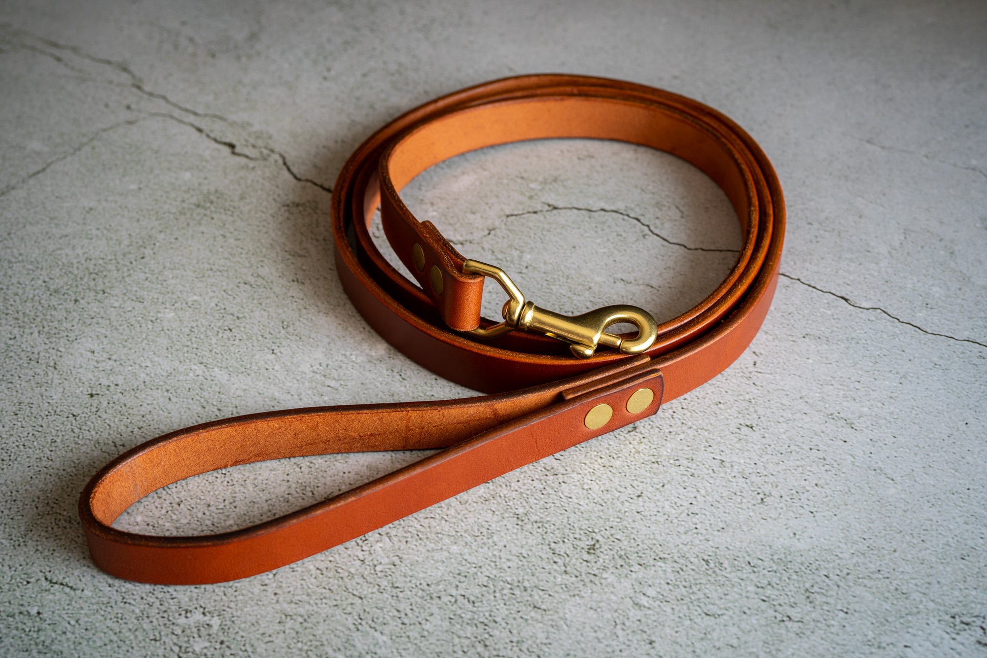 Handmade chestnut leather dog leash wrapped around itself. | Laisse pour chien en cuir de couleur châtaigne artisanale enroulée autour d'elle-même.