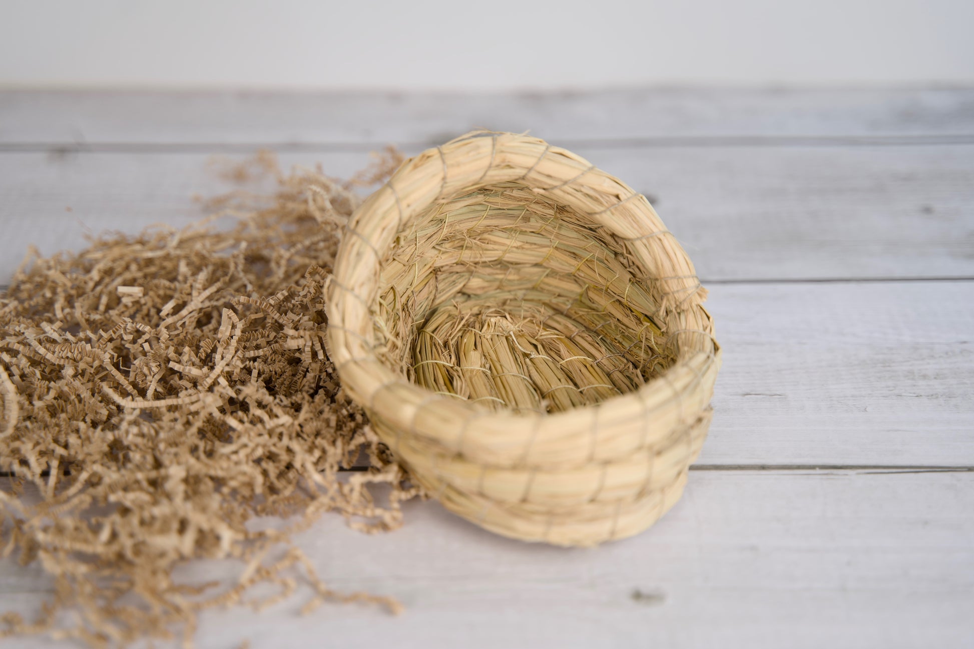Panier en paille tressée pour petits animaux, posé sur une surface en bois.