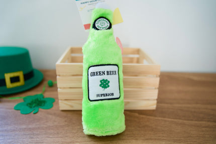 Jouet pour chien en peluche verte en forme de bouteille avec une étiquette Green Beer Superior sur une surface en bois.