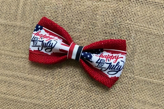 Pet bow tie with 'Happy 4th of July' text on a textured fabric background.|Nœud papillon pour chien avec l'inscription « Happy 4th of July » sur un fond brun texturé.