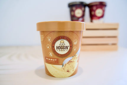 Un pot de glace au beurre de cacahuète Hoggin' Dogs posé sur une surface blanche, avec un arrière-plan flou.
