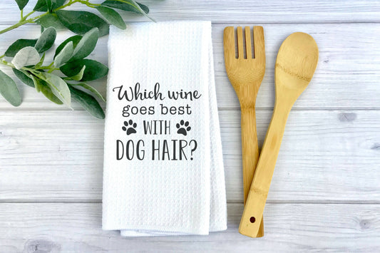 Pet-themed kitchen white towel with text 'Which wine goes best with dog hair?' next to wooden utensils.|Torchon de cuisine blanc sur le thème des animaux, portant l'inscription « Quel vin s'accorde le mieux avec les poils de chien ? », placé à côté d'ustensiles en bois.