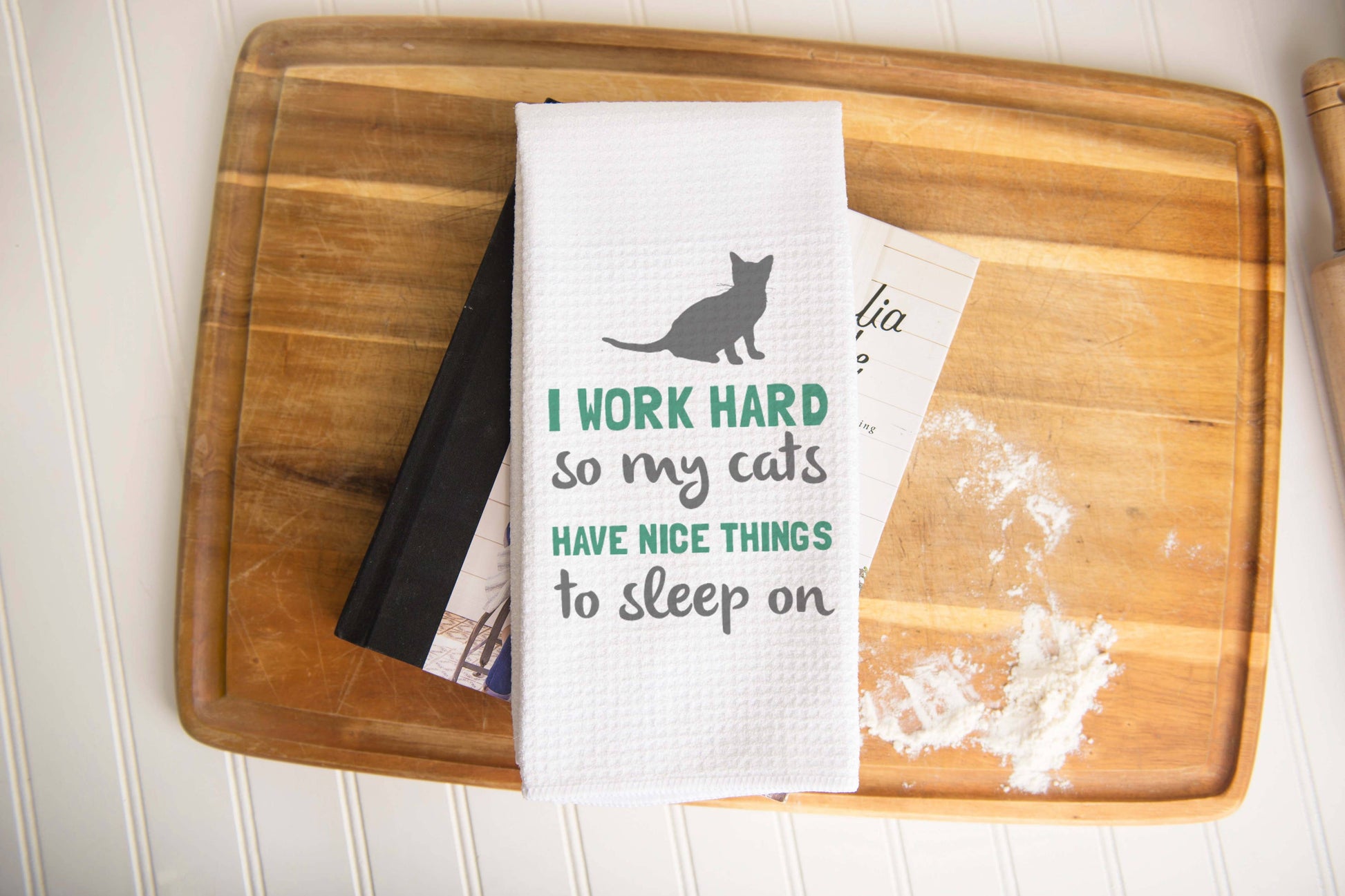 Torchon de cuisine blanc sur le thème des chats, avec texte et motif de chat, posé sur une planche en bois.