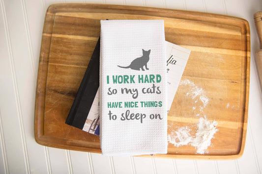 Cat-themed kitchen white towel with text and cat graphic on a wooden board.|Torchon de cuisine blanc sur le thème des chats, avec texte et motif de chat, posé sur une planche en bois.