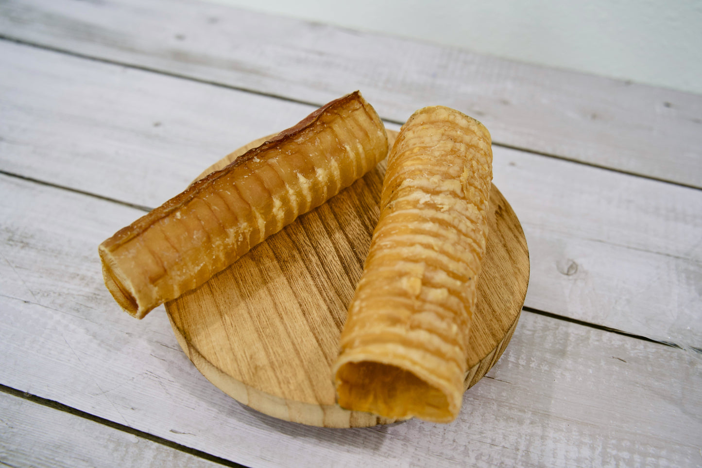 Two large crispy beef trachea for dogs on a round wooden board.