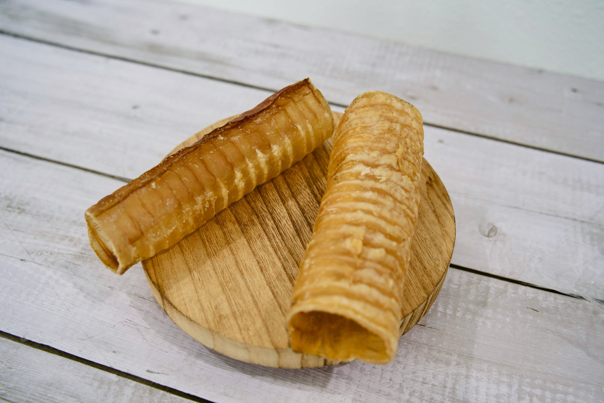 Two large crispy beef trachea for dogs on a round wooden board.
