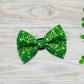 Green dog bow tie with shamrock pattern on a wooden surface with clover leaves.
