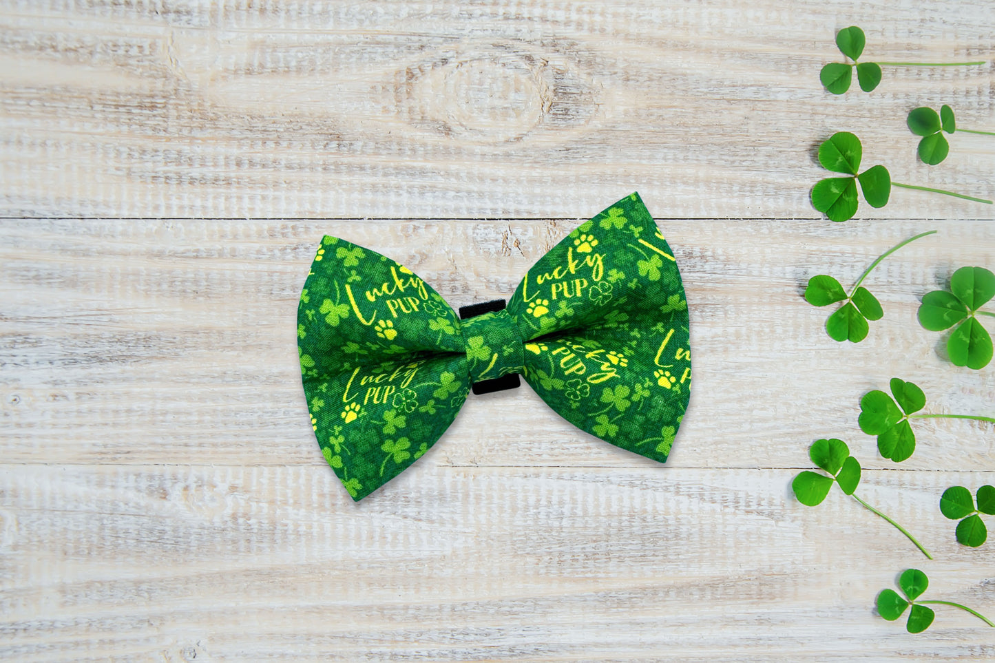 Green dog bow tie with shamrock pattern on a wooden surface with clover leaves.