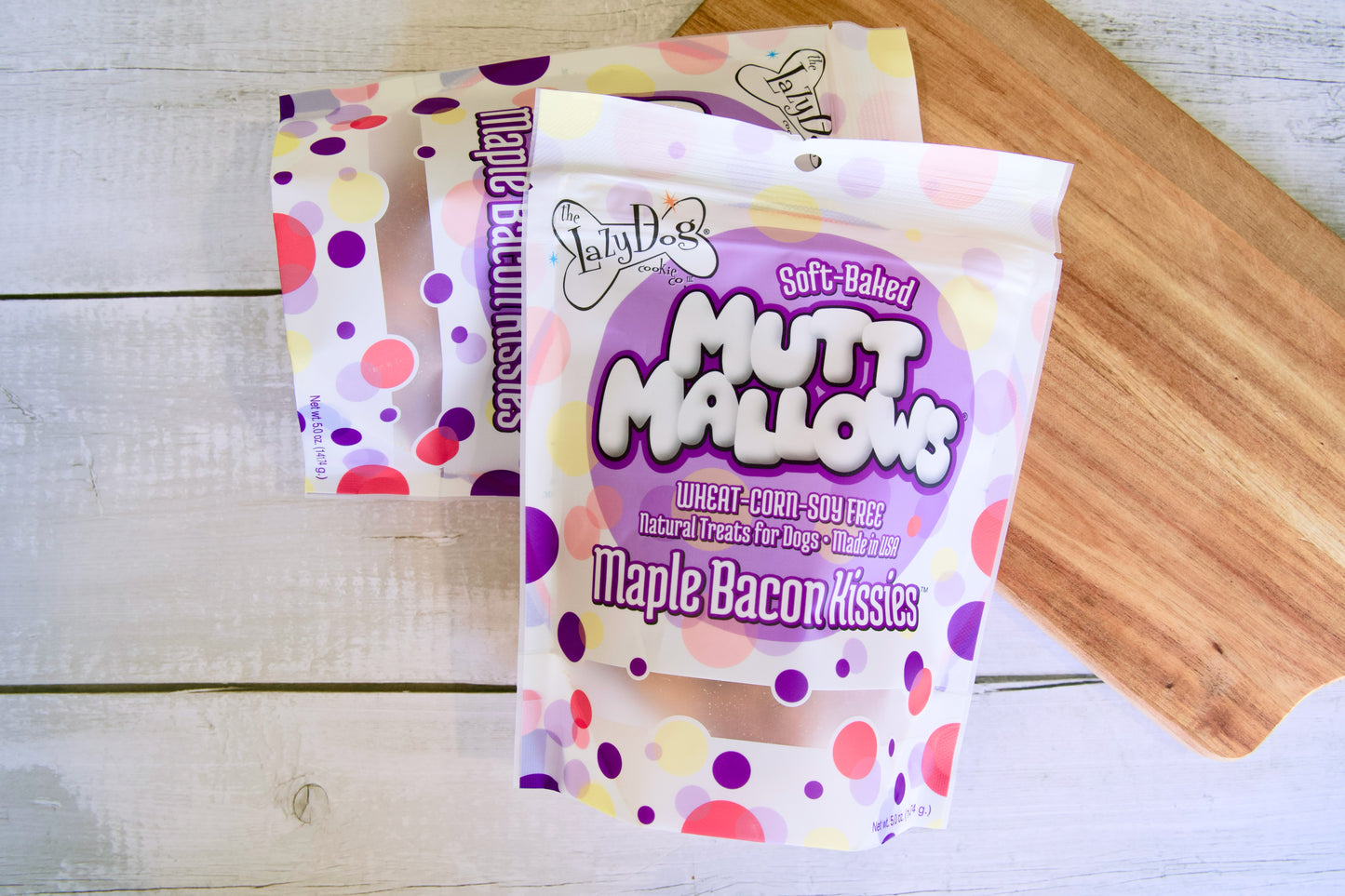 Packets of Mutt Mallows maple bacon kisses for dogs on a wooden surface.