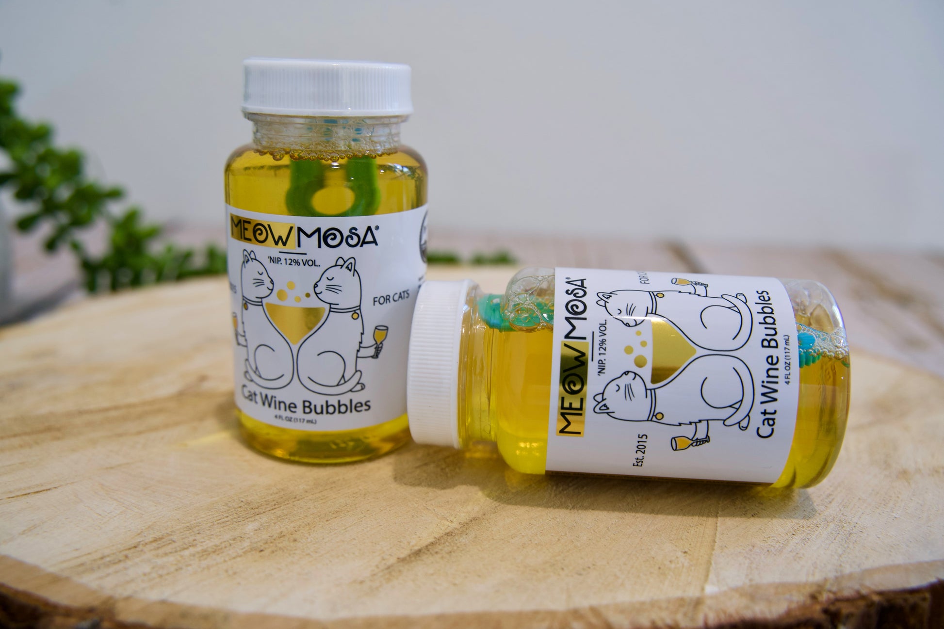 Deux bouteilles de vin pétillant pour chats « Mew & Moos » posées sur une surface en bois, avec un arrière-plan flou.