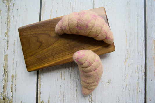 Two croissant-shaped wool dog toys in a light beige color with pink stripes.|Deux jouets pour chiens en laine en forme de croissant, de couleur beige clair avec des rayures roses.