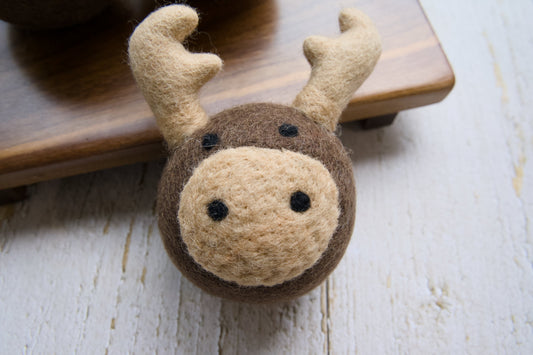 A wool reindeer head, ball for dogs on a wooden board.|Une tête de renne en laine et une balle pour chien sur un support en bois.