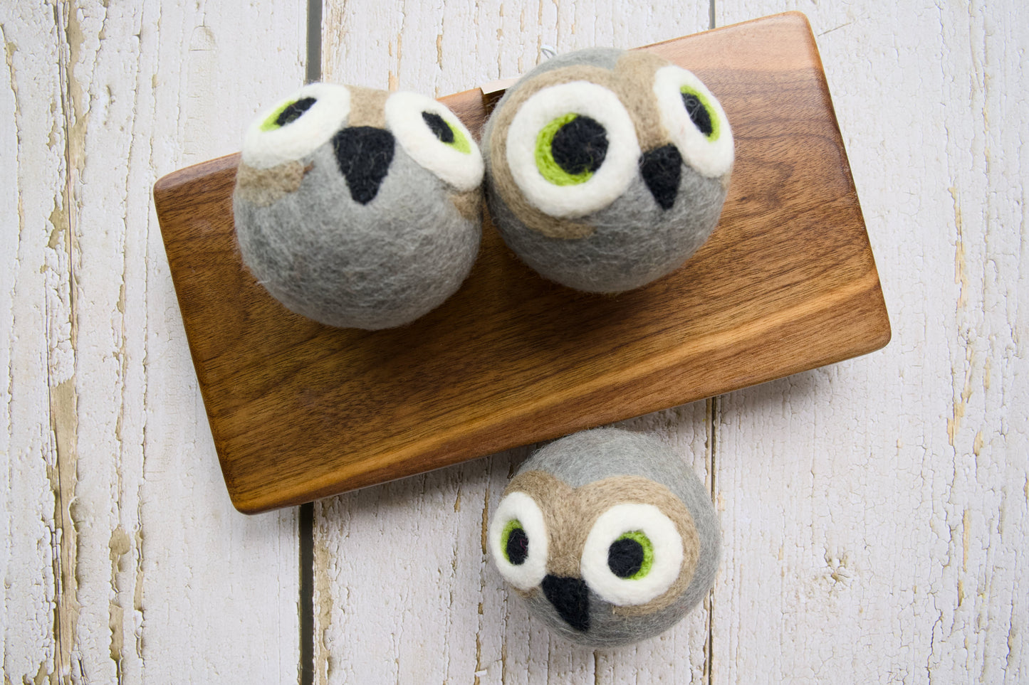 Three gray felt owl dog toys arranged on a wooden board.