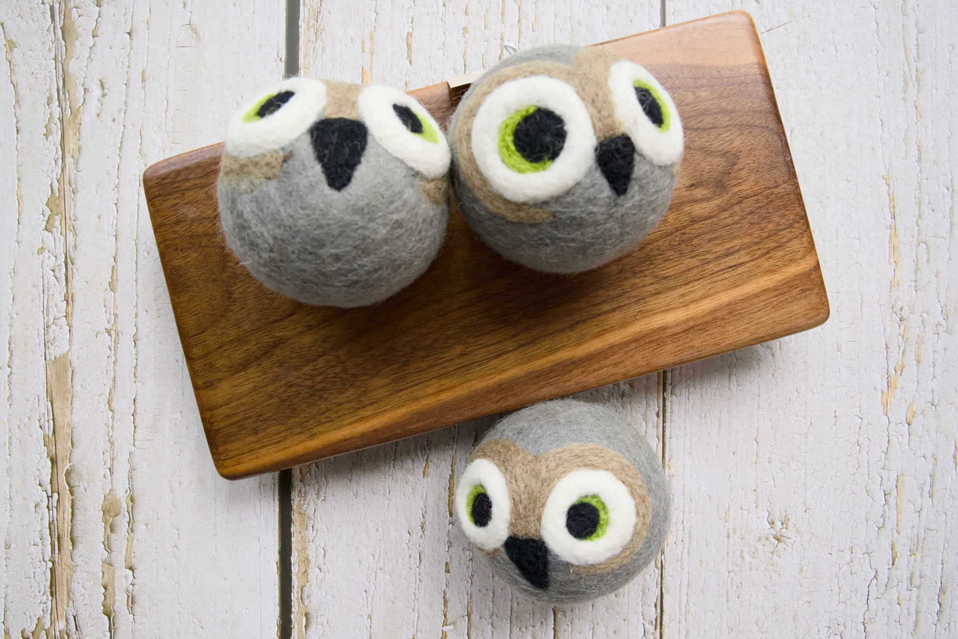 Three gray felt owl dog toys arranged on a wooden board.