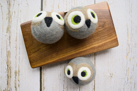 Three gray felt owl dog toys arranged on a wooden board.|Trois jouets pour chiens en forme de hibou, en feutrine grise, disposés sur une planche en bois.