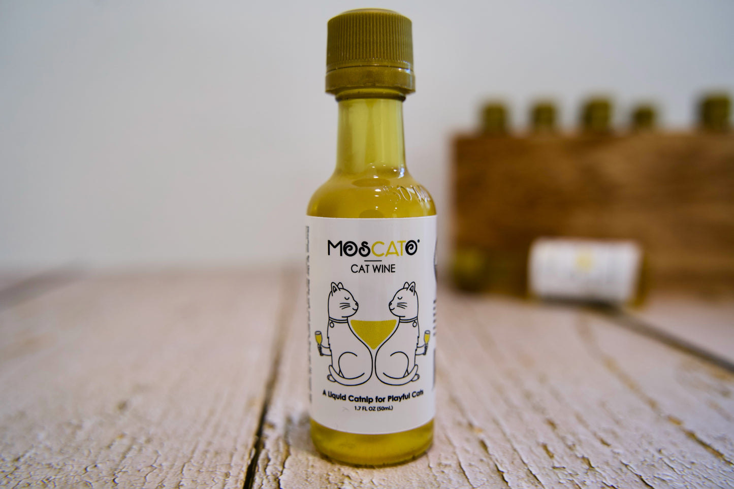 Bouteille de vin pour chats MosCato posée sur une surface en bois, avec un arrière-plan flou.